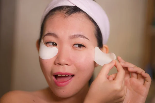 Jeune belle et heureuse Asiatique Japonais femme souriant à miroir de salle de bains appliquant des patchs hydratants sous les yeux dans les cosmétiques de beauté et soins de la peau du visage — Photo