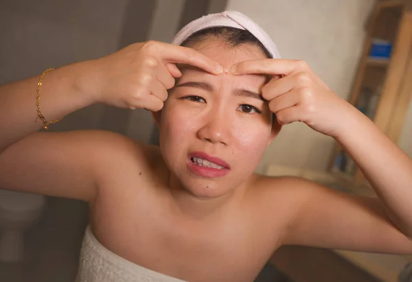 Estilo de vida cara retrato de joven molesto y expresivo asiático chino mujer apretando espinillas mientras mira el espejo en el baño en el cuidado de la piel facial y la belleza — Foto de Stock