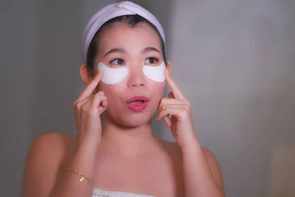 Wanita muda Cina cantik dan bahagia tersenyum ke kamar mandi cermin menerapkan tambalan mata terhidrasi di bawah mata dalam kosmetik kecantikan dan perawatan kulit wajah — Stok Foto