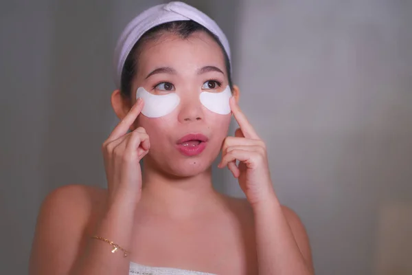 Jeune belle et heureuse asiatique femme chinoise souriant au miroir de salle de bains appliquant des patchs hydratants sous les yeux dans les cosmétiques de beauté et soins de la peau du visage — Photo