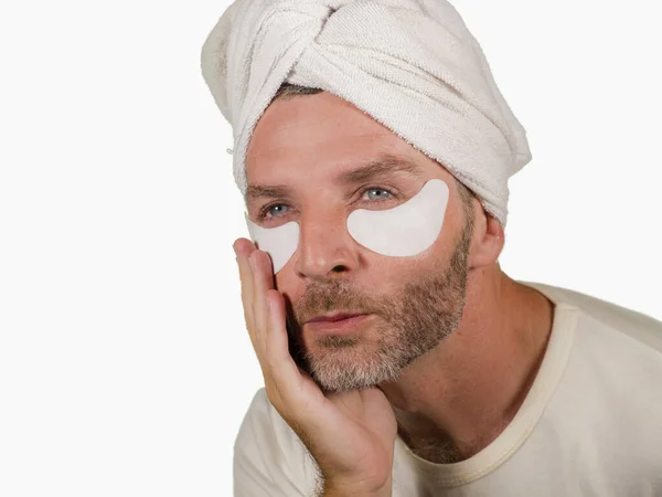 Śmieszne odizolowane twarz portret młody szczęśliwy i atrakcyjny obóz gej człowiek stosując nawilżający oko patch twarzy produkt z głowa owinięte ręcznik w męskiej pielęgnacji skóry — Zdjęcie stockowe