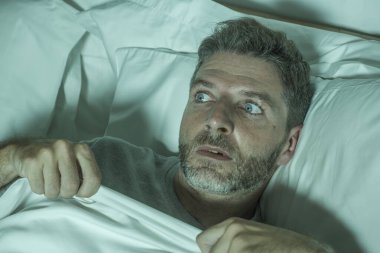  stressed and scared man alone in bed awake at night in fear after having a nightmare feeling paranoid holding the blanket in funny panic face expression  clipart