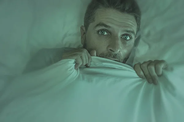 Homem estressado e assustado sozinho na cama acordado à noite com medo depois de ter um pesadelo se sentindo paranóico segurando o cobertor na expressão engraçado rosto de pânico — Fotografia de Stock