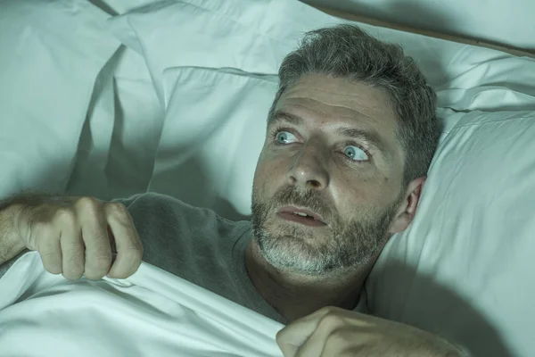 Stresszes és ijedt férfi egyedül az ágyban ébren éjjel a félelem, miután egy rémálom érzés paranoid tartja a takarót vicces pánik arckifejezés — Stock Fotó