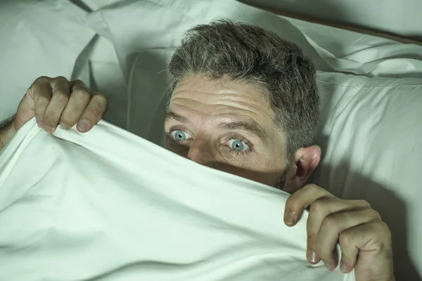 Stresszes és ijedt férfi egyedül az ágyban ébren éjjel a félelem, miután egy rémálom érzés paranoid tartja a takarót vicces pánik arckifejezés — Stock Fotó
