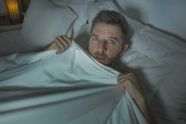 Homem estressado e assustado sozinho na cama acordado à noite com medo depois de ter um pesadelo se sentindo paranóico segurando o cobertor na expressão engraçado rosto de pânico — Fotografia de Stock