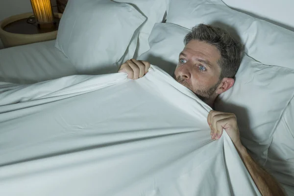 Estresado y asustado hombre solo en la cama despierto por la noche con miedo después de tener una pesadilla sensación paranoica sosteniendo la manta en expresión de pánico cara divertida — Foto de Stock