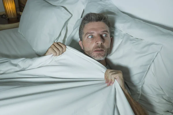 Estresado y asustado hombre solo en la cama despierto por la noche con miedo después de tener una pesadilla sensación paranoica sosteniendo la manta en expresión de pánico cara divertida —  Fotos de Stock
