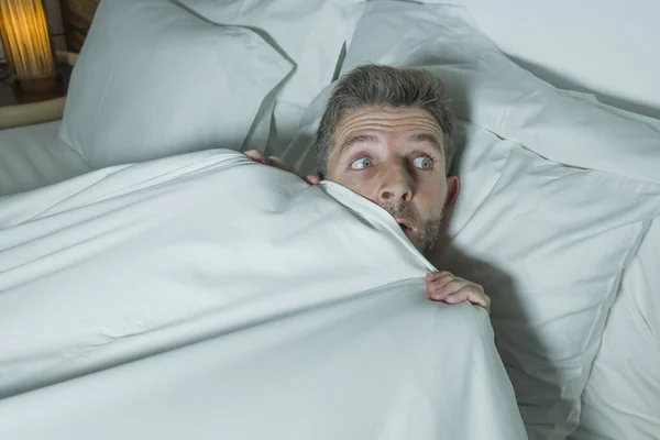 Homem estressado e assustado sozinho na cama acordado à noite com medo depois de ter um pesadelo se sentindo paranóico segurando o cobertor na expressão engraçado rosto de pânico — Fotografia de Stock