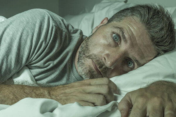 dramatic portrait of stressed and frustrated man in bed awake at night suffering insomnia sleeping disorder tired and desperate unable sleep feeling exhausted 