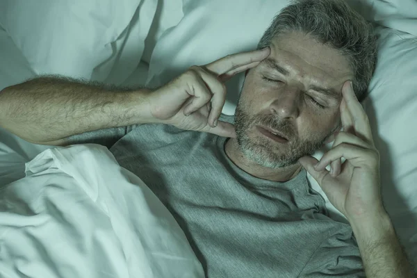 Dramático retrato del hombre estresado y frustrado en la cama despierto por la noche que sufre de insomnio trastorno del sueño cansado y desesperado incapaz de dormir sensación agotada — Foto de Stock