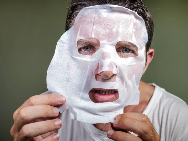 Lifestyle απομονωμένο πορτρέτο του νεαρού παράξενο και αστείο άνδρα στο σπίτι προσπαθεί να χρησιμοποιήσει χαρτί καθαρισμού μάσκα προσώπου εφαρμογή αντι γήρανση θεραπεία ομορφιάς — Φωτογραφία Αρχείου