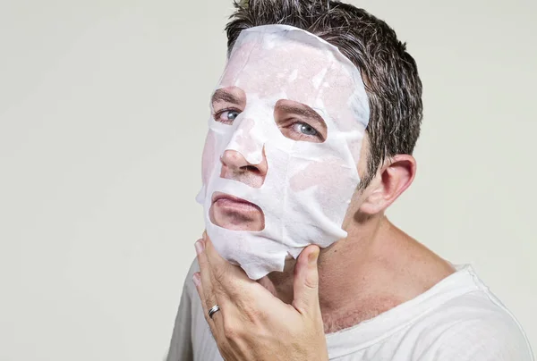 Estilo de vida isolado fundo retrato de jovem estranho e engraçado homem em casa tentando usar papel máscara facial limpeza aplicando tratamento de beleza anti envelhecimento — Fotografia de Stock