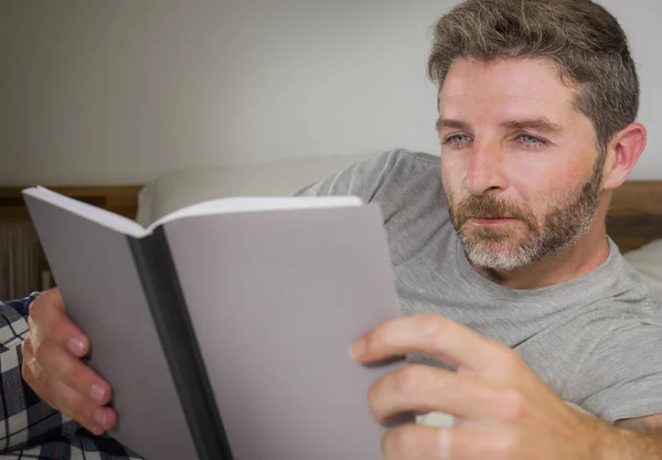 Mode de vie portrait de jeune homme séduisant et détendu à la maison couché confortablement sur le lit en pyjama lire un livre en profitant d'un roman intéressant frais et confortable — Photo