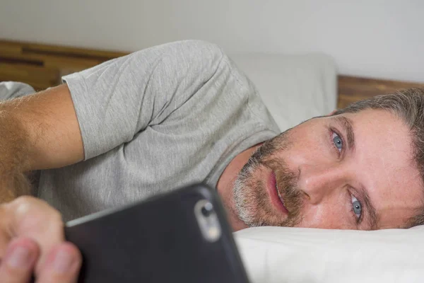 Portrait de style de vie domestique de jeune homme heureux et attrayant allongé sur le lit à la maison souriant gai et détendu en utilisant le réseautage de téléphonie mobile satisfait portant un pyjama — Photo