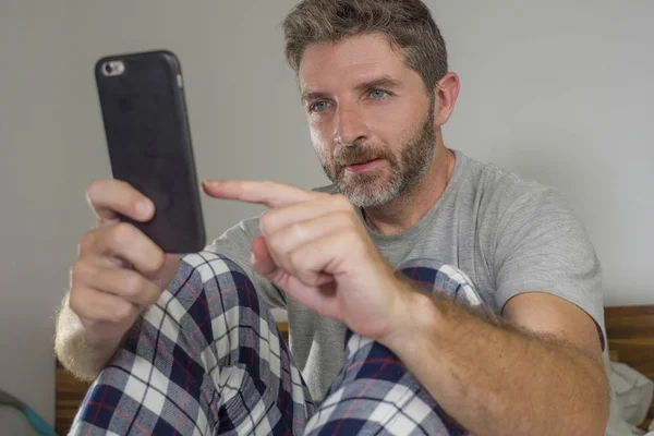 Portrait de style de vie domestique de jeune homme heureux et attrayant allongé sur le lit à la maison souriant gai et détendu en utilisant le réseautage de téléphonie mobile satisfait portant un pyjama — Photo