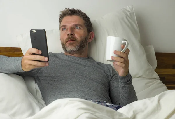 Portrait de style de vie domestique de jeune homme réfléchi et attrayant couché sur le lit à la maison pensant et rêvant détendu en utilisant le réseau de téléphonie mobile portant un pyjama — Photo