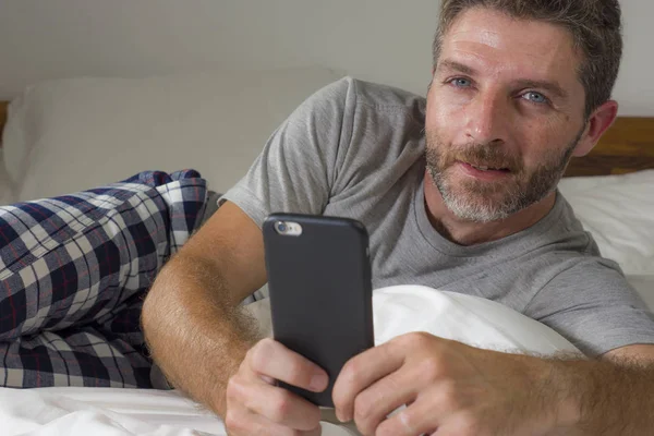 Stile di vita domestico ritratto di giovane uomo felice e attraente sdraiato sul letto a casa sorridente allegro e rilassato utilizzando la rete di telefonia mobile soddisfatto indossando pigiama — Foto Stock