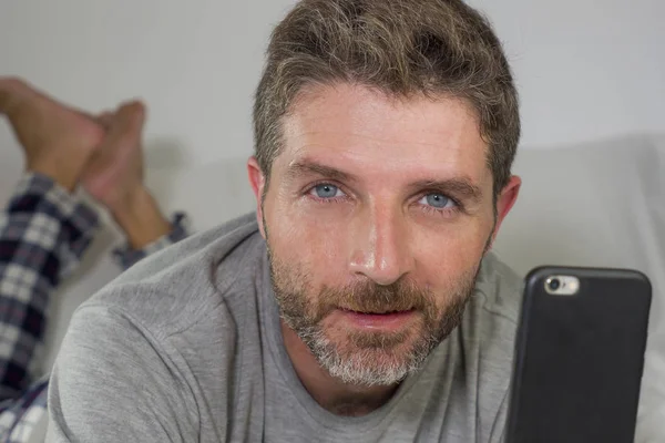 Retrato do estilo de vida doméstico de homem jovem feliz e atraente deitado na cama em casa sorrindo alegre e relaxado usando rede de telefone móvel satisfeito vestindo pijama — Fotografia de Stock