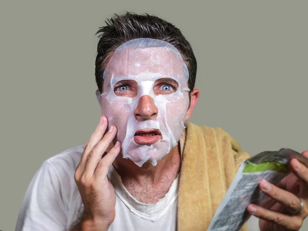 Νεαρός περίεργος και αστείος άνθρωπος στο σπίτι προσπαθεί να χρησιμοποιήσει χαρτί καθαρισμού μάσκα προσώπου εφαρμογή αντι γήρανση θεραπεία προσώπου ανάγνωση οδηγίες προϊόν ομορφιάς — Φωτογραφία Αρχείου