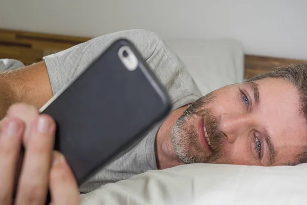 Portrait de style de vie domestique de jeune homme heureux et attrayant allongé sur le lit à la maison souriant gai et détendu en utilisant le réseautage de téléphonie mobile satisfait portant un pyjama — Photo