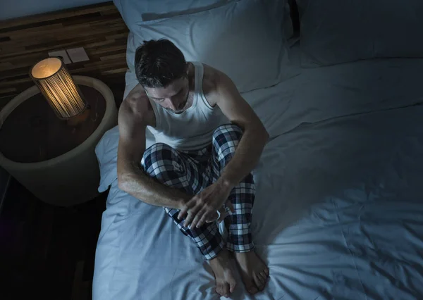 Dramatisches Lebensstil-Porträt eines jungen attraktiven, traurigen und depressiven Mannes, der nachts im Bett sitzt und sich gestresst und verzweifelt unter Depressionen leidet. — Stockfoto