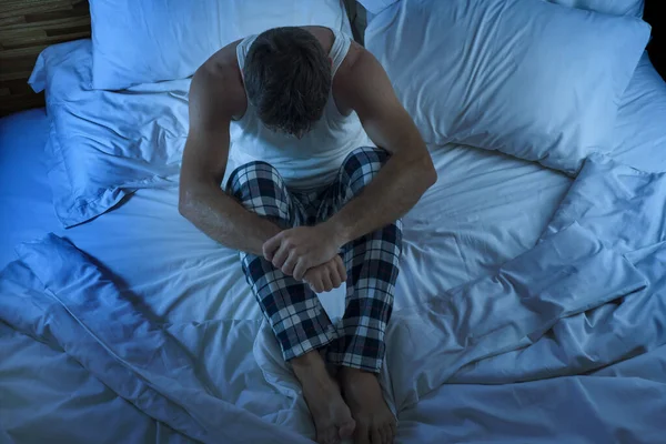 Dramatic lifestyle portrait of young attractive sad and depressed man sitting on bed at night feeling stressed and desperate suffering depression problem in sadness and pain — Stock Photo, Image