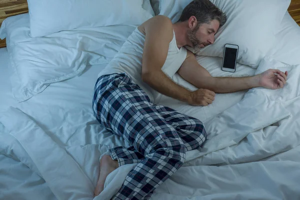 Estilo de vida doméstico alto ángulo retrato de hombre joven atractivo y cansado durmiendo en la cama celebración de teléfono móvil en Internet y la adicción a las redes sociales y el uso excesivo de la red — Foto de Stock