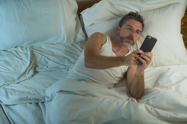 Estilo de vida doméstico retrato de alto ângulo de homem jovem atraente e relaxado em casa deitado na cama vestindo pijama usando rede de telefonia móvel e olhando para as mídias sociais — Fotografia de Stock