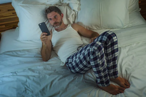 Stile di vita domestico ritratto ad alto angolo di giovane uomo attraente e rilassato a casa sdraiato sul letto indossando pigiami utilizzando la rete di telefonia mobile e guardando i social media — Foto Stock