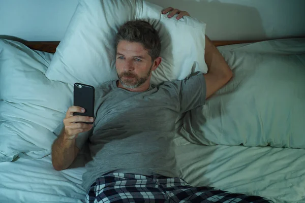 Estilo de vida doméstico retrato de alto ângulo de homem jovem atraente e relaxado em casa deitado na cama vestindo pijama usando rede de telefonia móvel e olhando para as mídias sociais — Fotografia de Stock