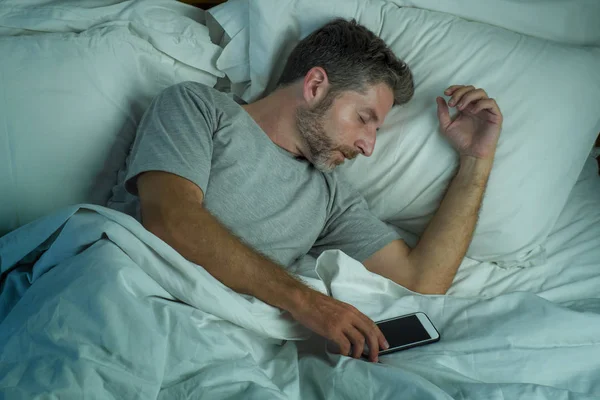 Domestic lifestyle high angle portrait of young attractive and tired man sleeping on bed holding mobile phone in internet and social media addiction and network overuse — Stock Photo, Image