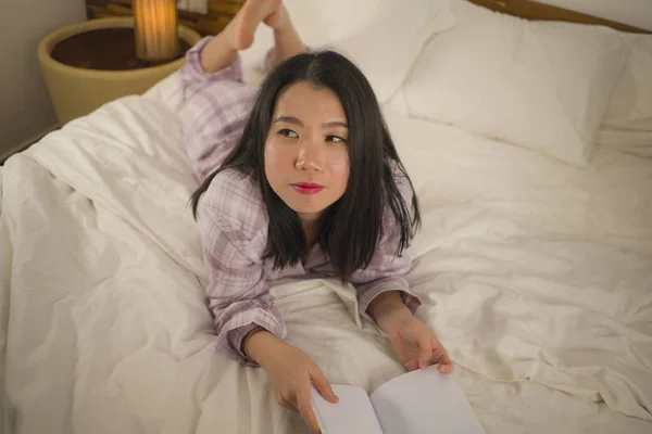 Молодая красивая и милая азиатская кореянка в постели читает книгу роман чувствуя себя счастливым и расслабленным или учиться дома в милых пижамах уютно и уютно — стоковое фото