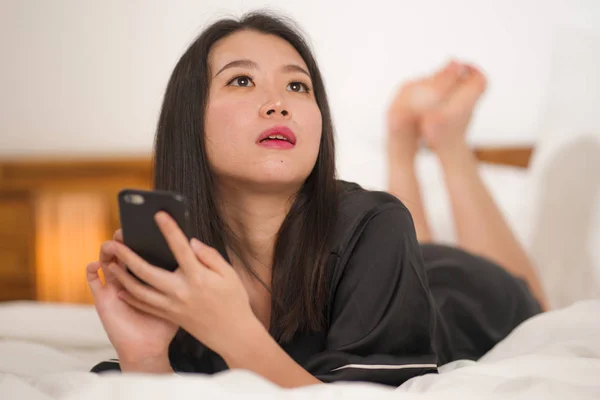 Jeune belle et douce asiatique coréen femme en chemise de nuit mignonne ludique au lit en utilisant un téléphone mobile appréciant les médias sociaux ou en ligne sortir ensemble app heureux et détendu — Photo