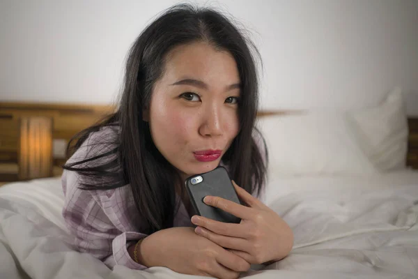 Jeune belle et douce asiatique coréen femme en pyjama mignon ludique au lit en utilisant un téléphone mobile profiter des médias sociaux ou en ligne sortir ensemble app heureux et détendu — Photo