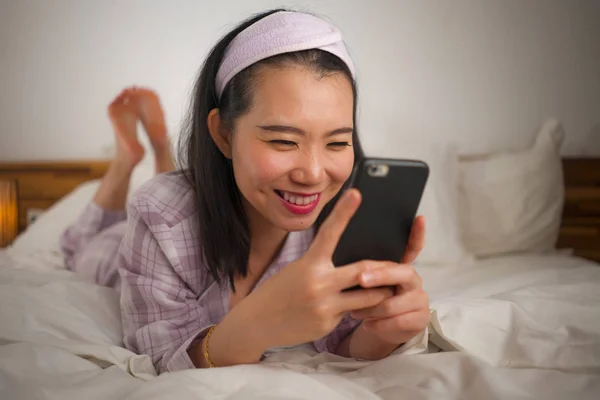 Jeune belle et douce asiatique coréen femme en pyjama mignon ludique au lit en utilisant un téléphone mobile profiter des médias sociaux ou en ligne sortir ensemble app souriant heureux et détendu — Photo