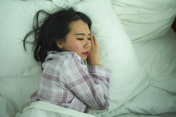 Lifestyleporträt einer jungen schönen und süßen asiatischen Chinesin in ihren 20er Jahren, die allein zu Hause schläft und entspannt im Schlafanzug auf dem Bett liegend glücklich und bequem ausruht — Stockfoto