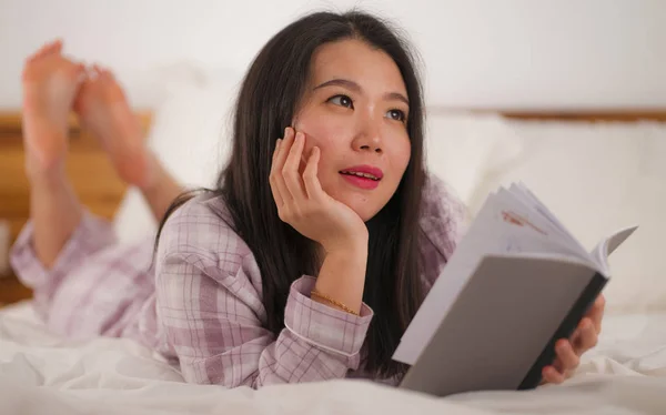 Genç, güzel ve tatlı Asyalı Çinli kadın kitap okuyor mutlu ve rahat hissediyor ya da evde güzel pijamalarıyla rahat ve rahat görünüyor. — Stok fotoğraf