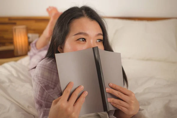 Junge schöne und süße asiatische Chinesin im Bett, die Buch-Roman liest, sich glücklich und entspannt fühlt oder zu Hause studiert und süße Pyjamas trägt, die gemütlich und heimelig aussehen — Stockfoto