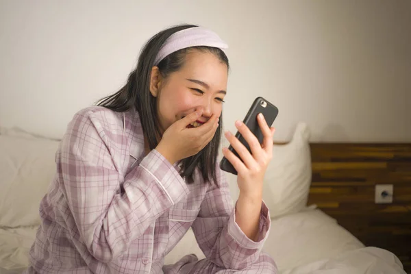Jeune belle et douce asiatique femme chinoise en pyjama mignon ludique au lit en utilisant un téléphone mobile profiter des médias sociaux ou en ligne sortir ensemble app heureux et détendu — Photo