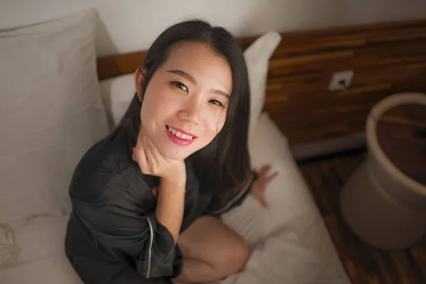 Молодая красивая и милая азиатская кореянка в постели чувствует себя счастливой и расслабленной в милой ночной рубашке наслаждаясь ленивым воскресным утром дома играя уютно — стоковое фото