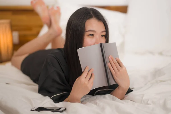 Jeune belle et douce asiatique coréen femme au lit lecture livre roman se sentir heureux et détendu ou étudier à la maison en chemise de nuit mignonne regardant confortable et accueillant — Photo