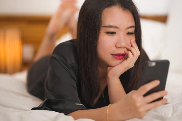 Jeune belle et douce asiatique coréen femme en chemise de nuit mignonne ludique au lit en utilisant un téléphone mobile appréciant les médias sociaux ou en ligne sortir ensemble app heureux et détendu — Photo