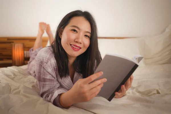 Genç ve güzel Asyalı kadın yatakta kitap okuyor mutlu ve neşeli hissediyor ya da evde sevimli pijamalarıyla rahat ve rahat görünüyor. — Stok fotoğraf