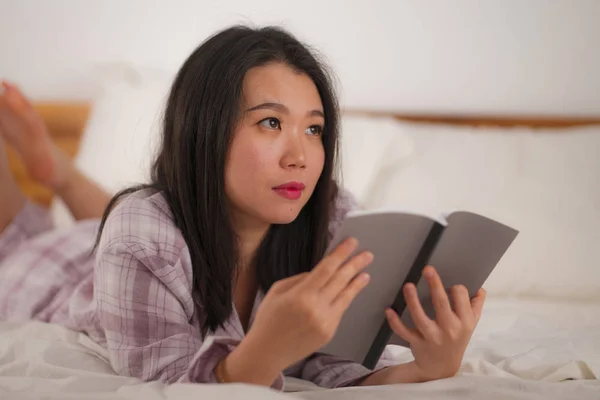 Jeune belle et douce Asiatique chinois femme au lit lecture livre roman se sentir heureux et ludique ou étudier à la maison en pyjama mignon regardant confortable et accueillant — Photo