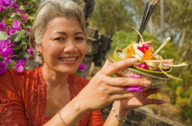 Bali Tapınağı 'nda elinde tütsü çubuğu ve çiçek sunan geleneksel Bali dini geleneği giymiş güzel ve mutlu Asyalı kadın. 