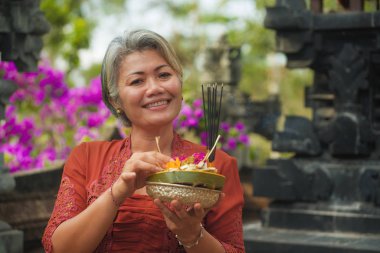 Bali Tapınağı 'nda elinde tütsü çubuğu ve çiçek sunan geleneksel Bali dini geleneği giymiş güzel ve mutlu Asyalı kadın. 
