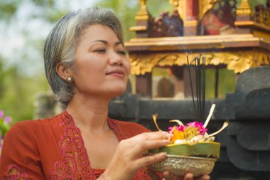Bali Tapınağı 'nda elinde tütsü çubuğu ve çiçek sunan geleneksel Bali dini geleneği giymiş güzel ve mutlu Asyalı kadın. 
