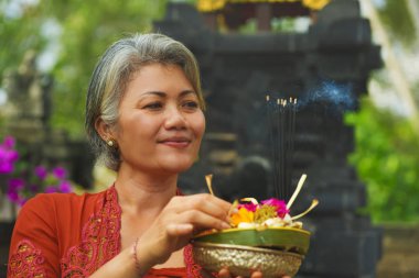 Bali Tapınağı 'nda elinde tütsü çubuğu ve çiçek sunan geleneksel Bali dini geleneği giymiş güzel ve mutlu Asyalı kadın. 