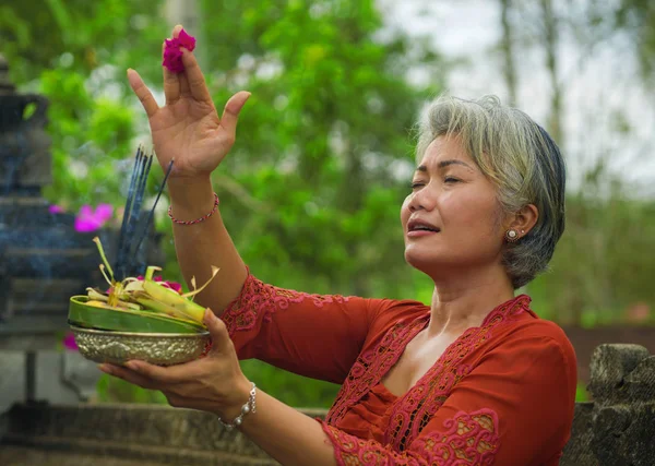 Bali Tapınağı 'nda elinde tütsü çubuğu ve çiçek sunan geleneksel Bali dini geleneği giymiş güzel ve mutlu Asyalı kadın. 